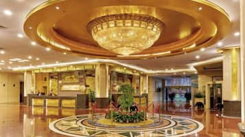 Un vestíbulo de hotel con un amplio mostrador de recepción circular, una lámpara de araña central y un suelo pulido.