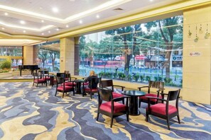 Un hall d’hôtel doté d’un tapis à motifs, d’un espace salon avec des fauteuils et des tables, d’un grand piano et de grandes fenêtres offrant une vue sur l’extérieur.
