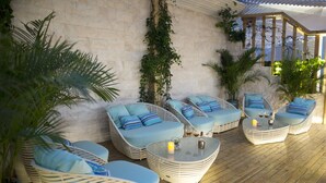 A covered outdoor seating area with wicker furniture and cushions, a glass table with candles, and potted plants. - Shantou International Hotel (Shantou)