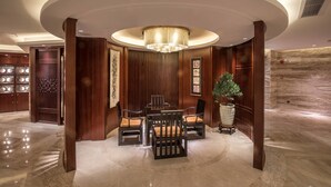 A lobby with a round table and chairs, a chandelier, wooden paneling, and a large vase with a plant. - Shantou International Hotel (Shantou)