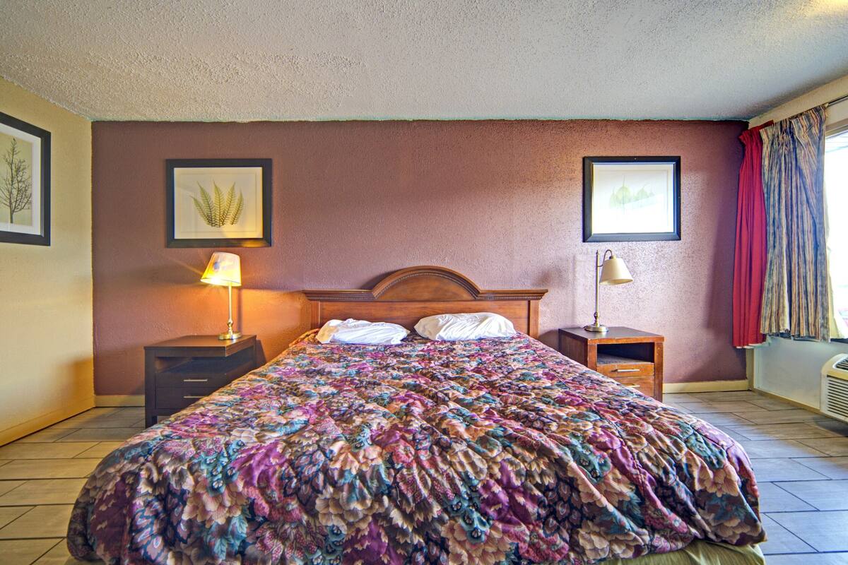 Un lit bien fait, recouvert d’une couvre-lit à motifs floraux, deux tables de chevet avec des lampes et des tableaux encadrés accrochés aux murs.