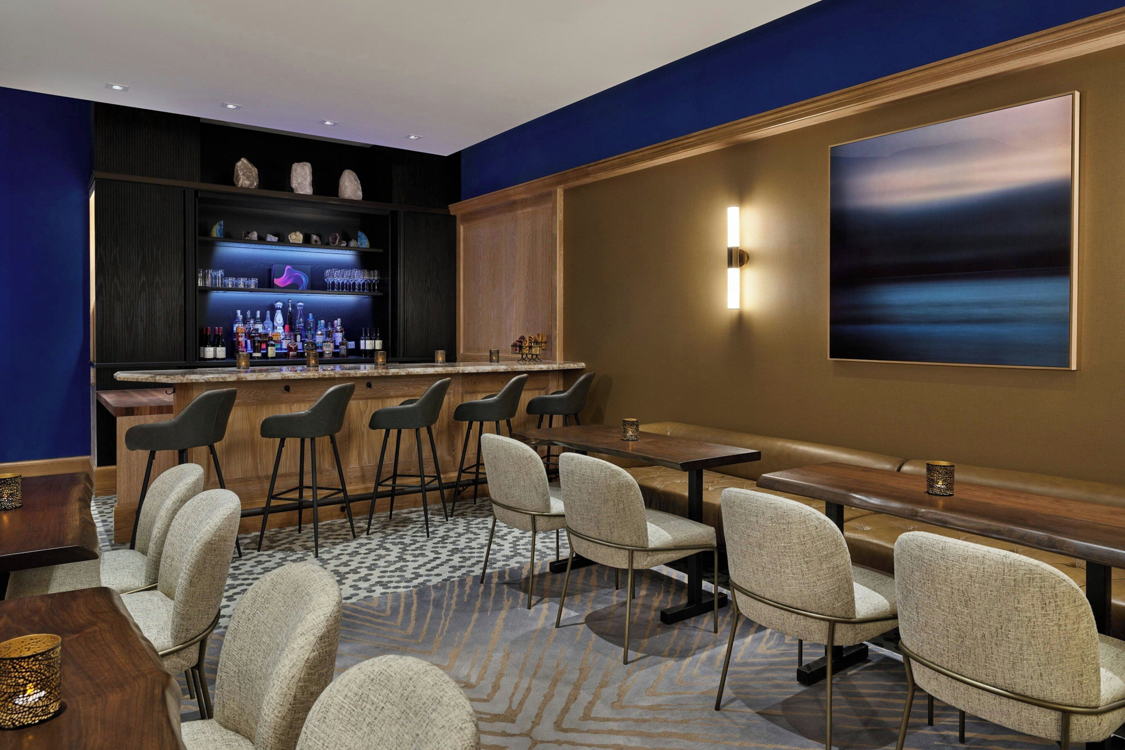 A bar area with stools and a long counter, a seating area with tables and chairs, and a large abstract painting on the wall.