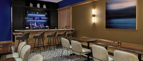 A bar area with stools and a long counter, a seating area with tables and chairs, and a large abstract painting on the wall.