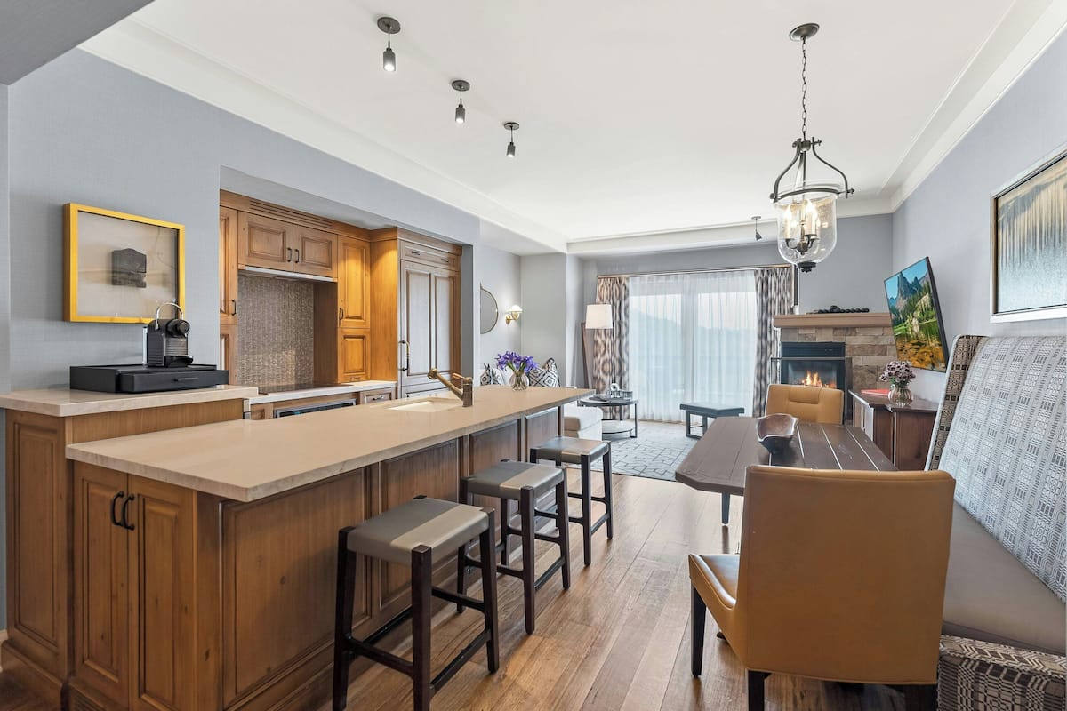 A modern kitchen with wooden cabinets, a large island with bar stools, and a dining area with a table and chairs.