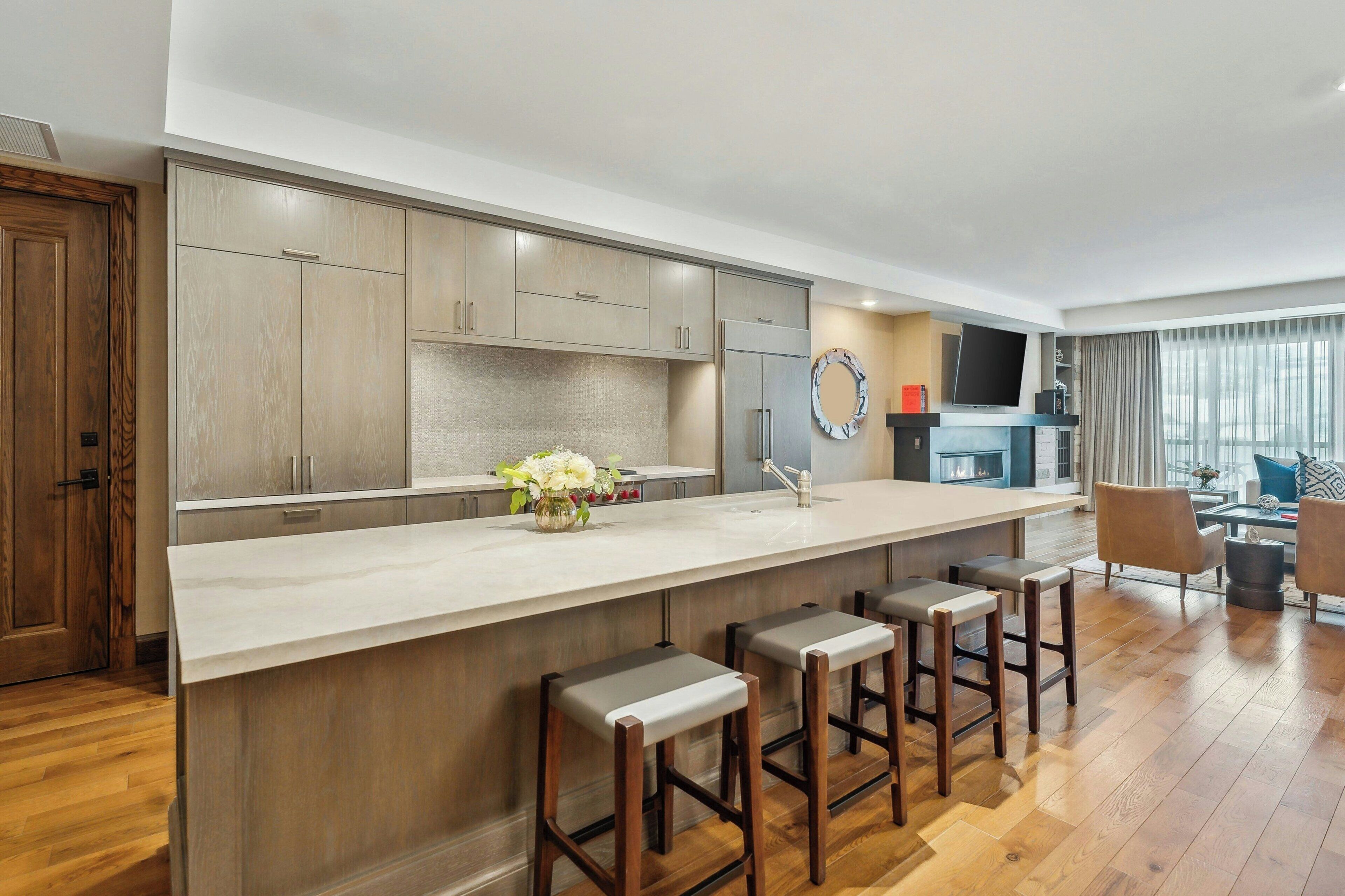 A modern kitchen with a large island, bar stools, and a dining area with a TV and seating.