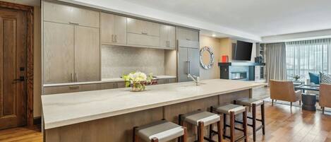 A modern kitchen with a large island, bar stools, and a dining area with a TV and seating.