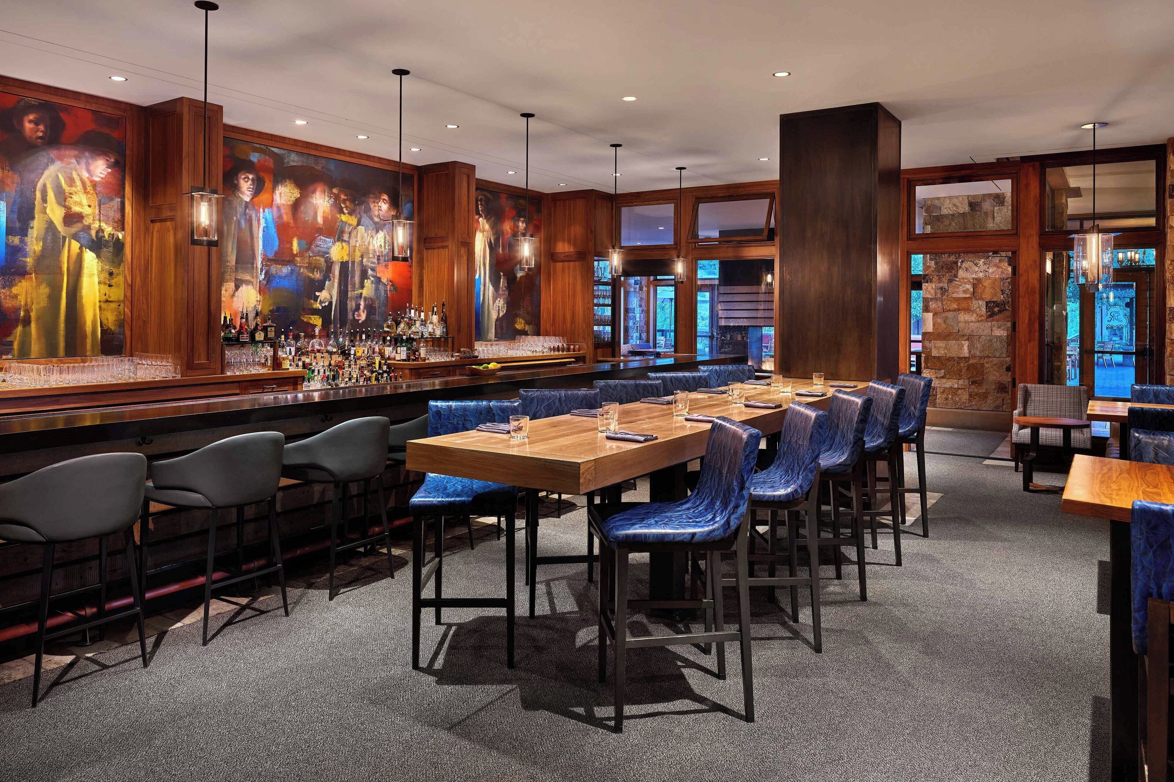 A bar area with a long counter, blue upholstered booths, and a large mural on the wall.