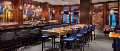 A bar area with a long counter, blue upholstered booths, and a large mural on the wall.