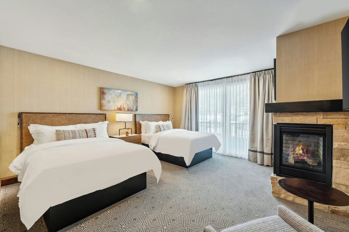 A hotel room with two beds, a fireplace, and a large window with curtains.