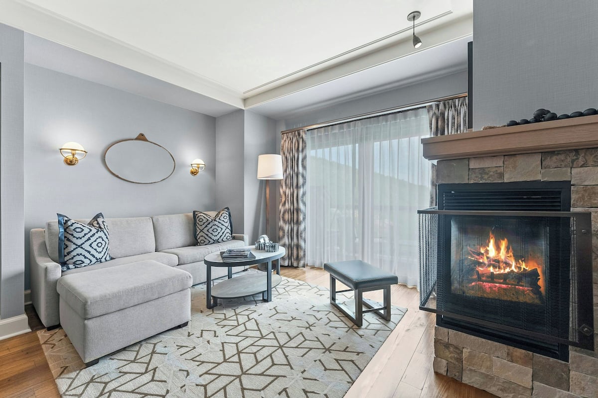 A modern living room with a fireplace, grey sofa, patterned rug, and a dining area.