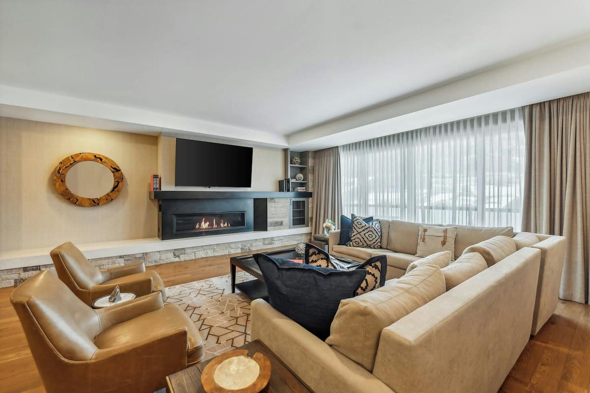 A modern living room with a fireplace, leather armchairs, a large sofa, and a flat-screen TV.
