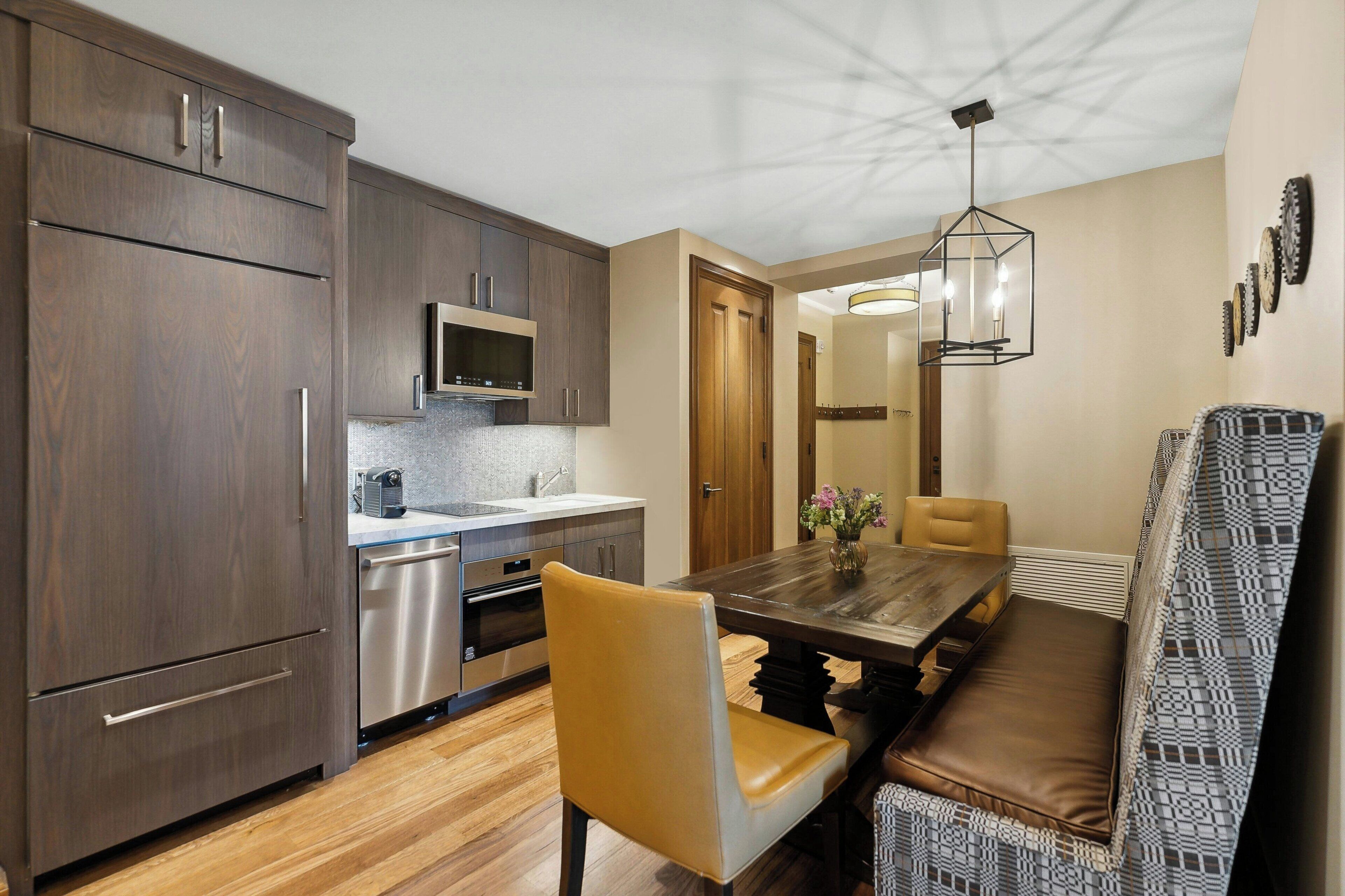 A modern kitchen with dark wood cabinets, stainless steel appliances, and a wooden dining table with a bench.