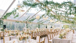 Um espaço para eventos coberto por tendas, com mesas montadas para um evento formal, com lustres e arranjos florais.