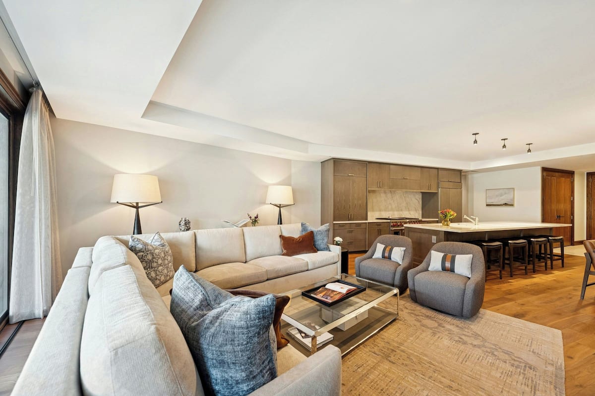 A modern living room with a sofa, armchairs, a coffee table, and a kitchen area with a bar.