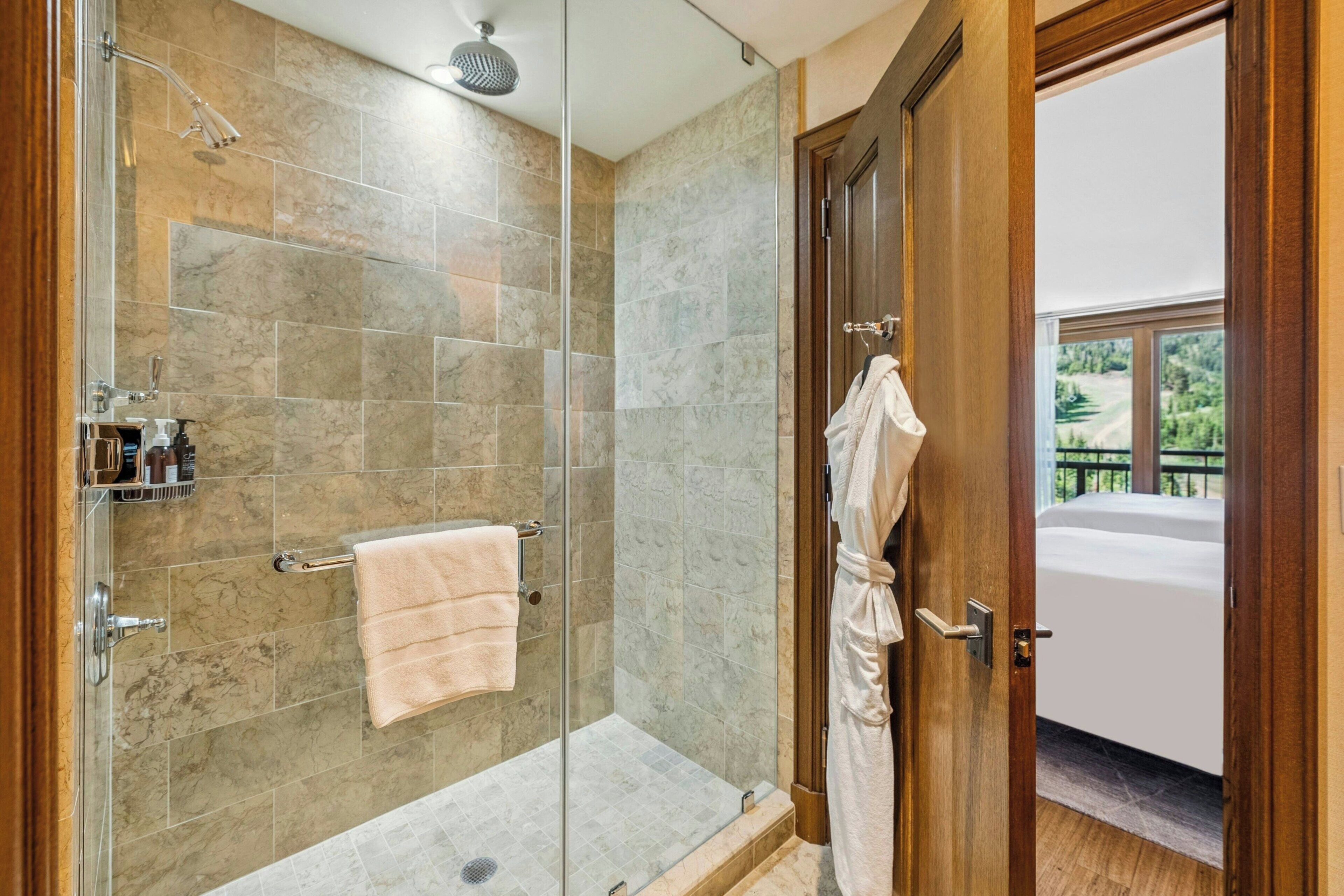 Une salle de bain moderne avec une douche en verre, des carreaux de marbre, un porte-serviettes et une porte en bois donnant sur un balcon avec vue.