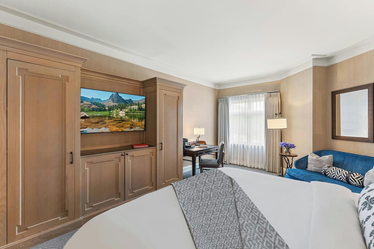 A hotel room with a large bed, a desk, a television, and a view of mountains.