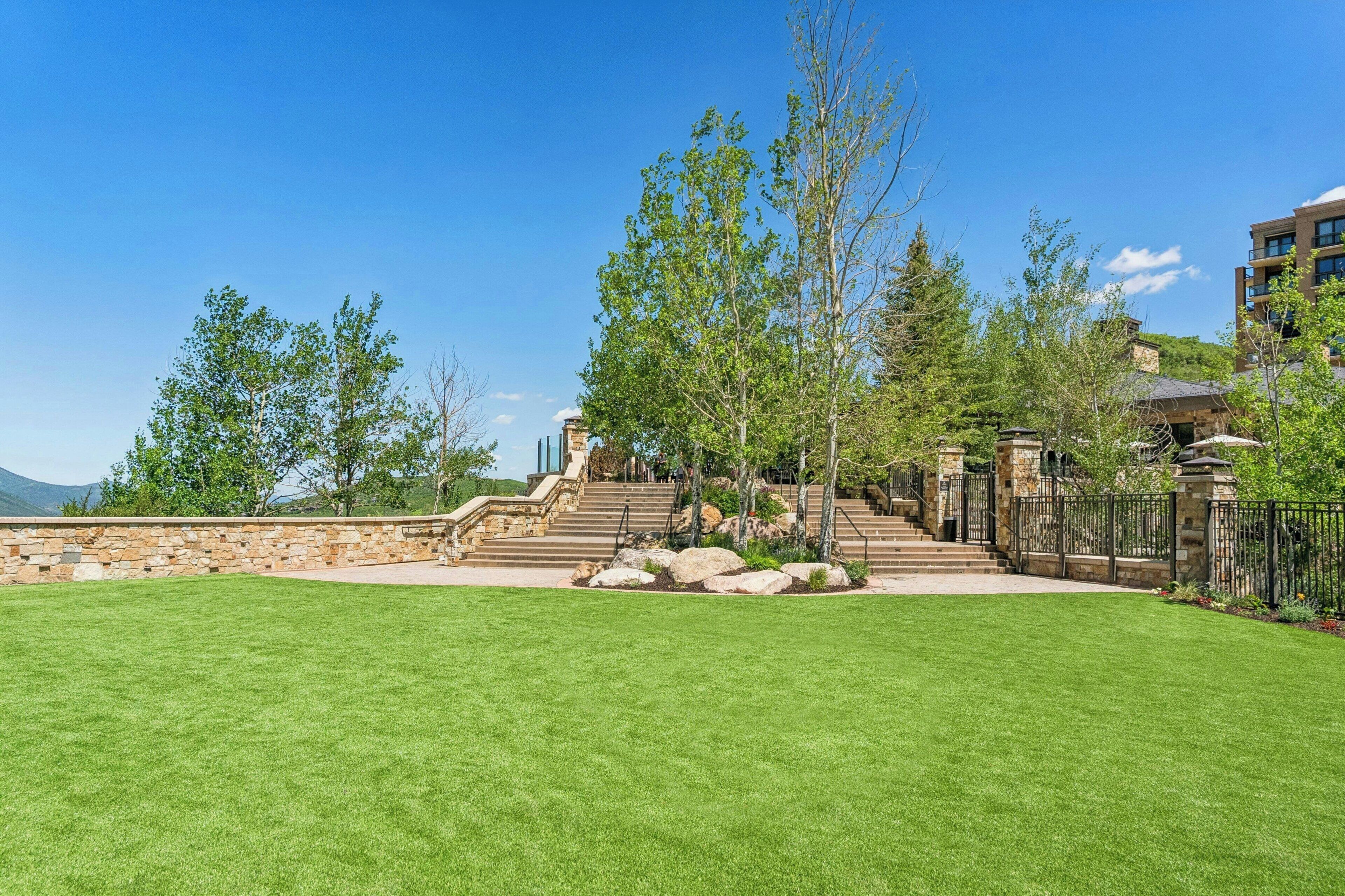 A well-maintained lawn, stone steps leading to a building, and a clear blue sky.