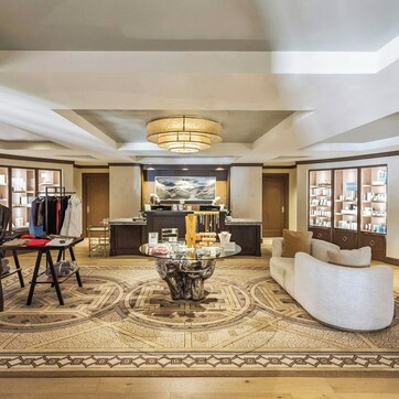 Un amplio vestíbulo de hotel con una zona de estar central, una recepción y una exhibición de batas y toallas.