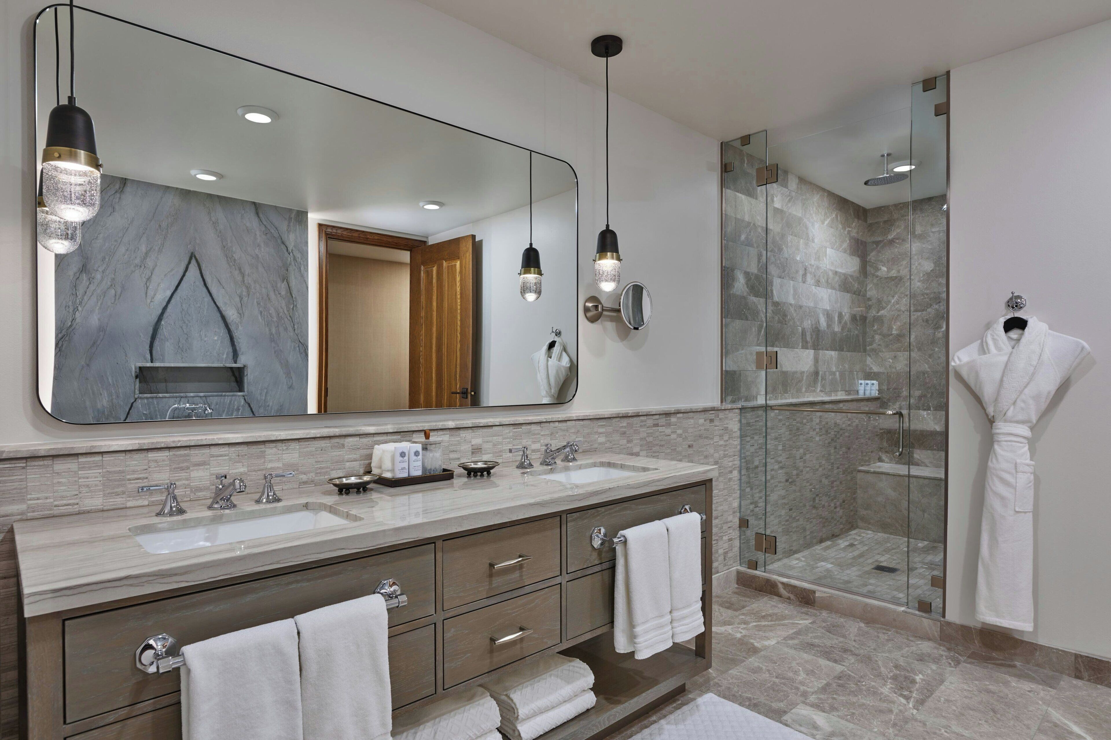 A modern bathroom with dual sinks, a large mirror, and a glass-enclosed shower.