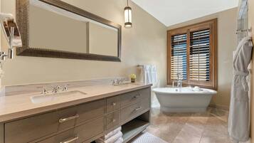 Un baño con tocador doble, un espejo grande, una bañera independiente y persianas de madera en la ventana.