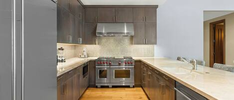 Una cocina moderna con armarios de madera oscura, electrodomésticos de acero inoxidable y encimera de color claro.