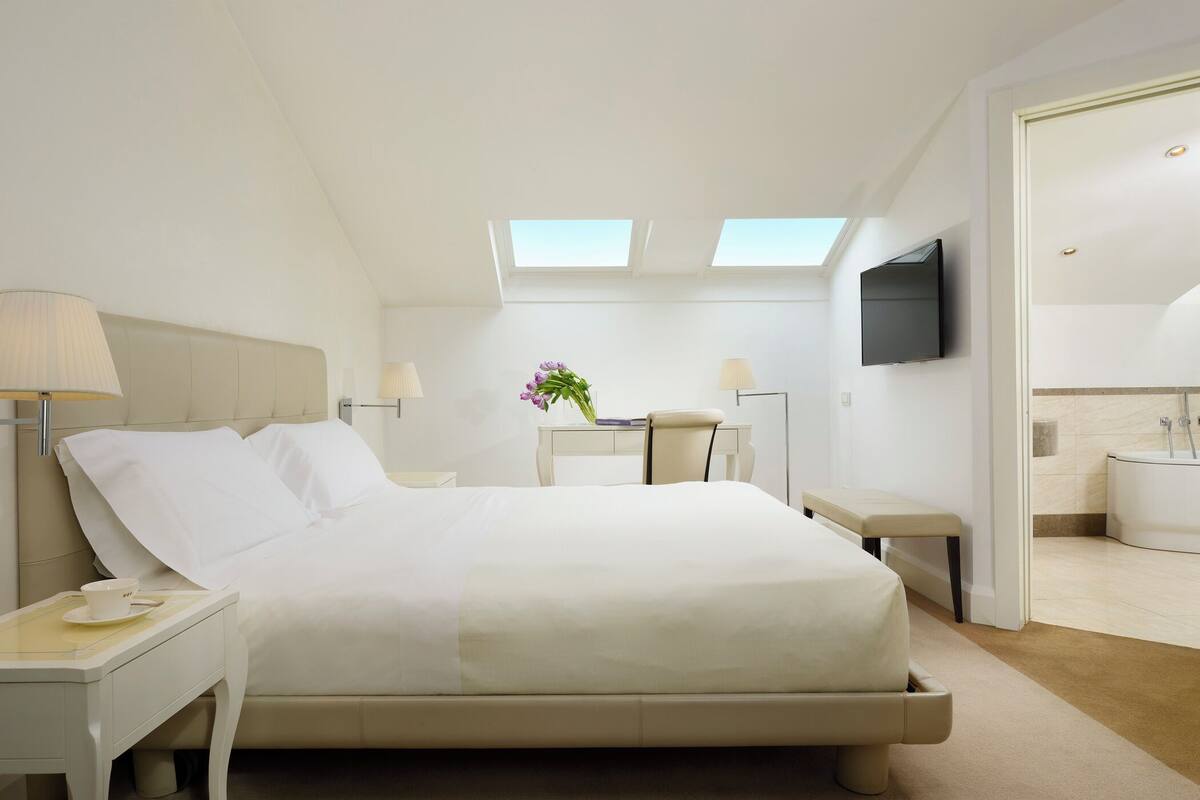 Une chambre d’hôtel moderne, dotée d’un grand lit, d’un bureau, d’une chaise, d’une télévision et d’une salle de bain visible à travers une porte ouverte.