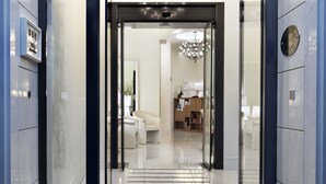 Una entrada de hotel moderna con puerta de vidrio, un mostrador de recepción y una araña visible en el interior.
