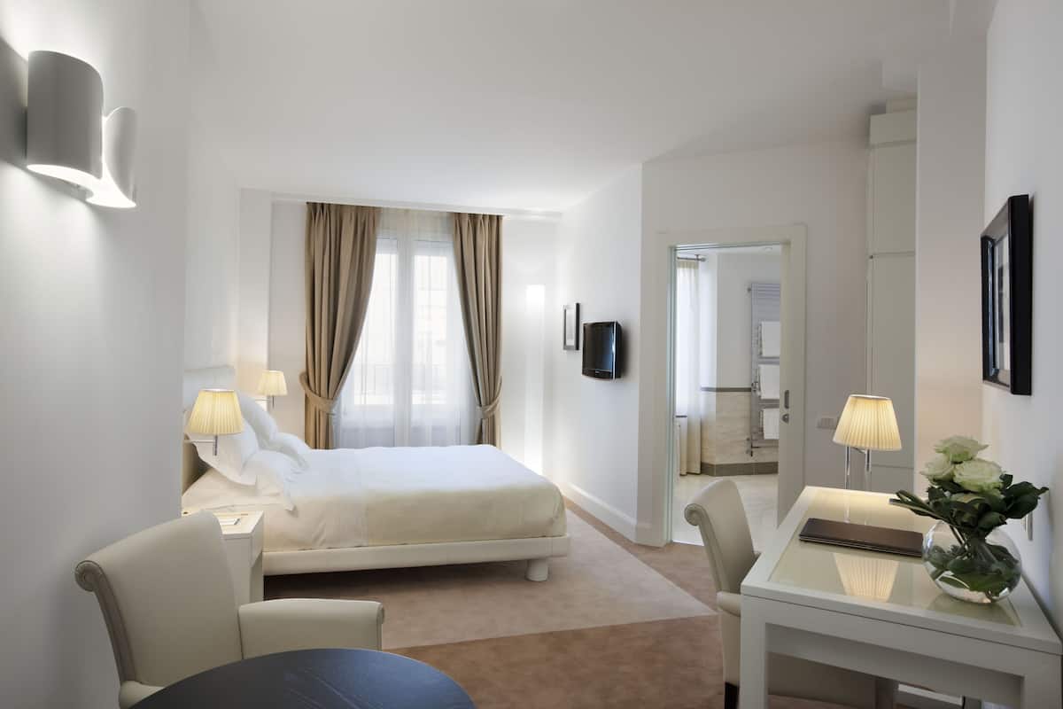 Une chambre d’hôtel moderne, équipée d’un lit, d’un bureau, d’une chaise et d’une table. Un téléviseur est fixé au mur et un vase rempli de fleurs est posé sur la table.