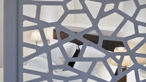 Una habitación con cama, mesitas de noche y un separador decorativo con motivos geométricos.