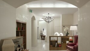 Un moderno vestíbulo de hotel con una araña, un sillón de cuero rojo, un mostrador de recepción de madera y una estantería con diversos objetos.
