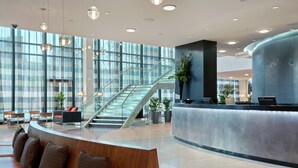 A modern lobby with a reception desk, seating area, staircase, and large windows. - Hilton Liverpool City Centre (Liverpool)