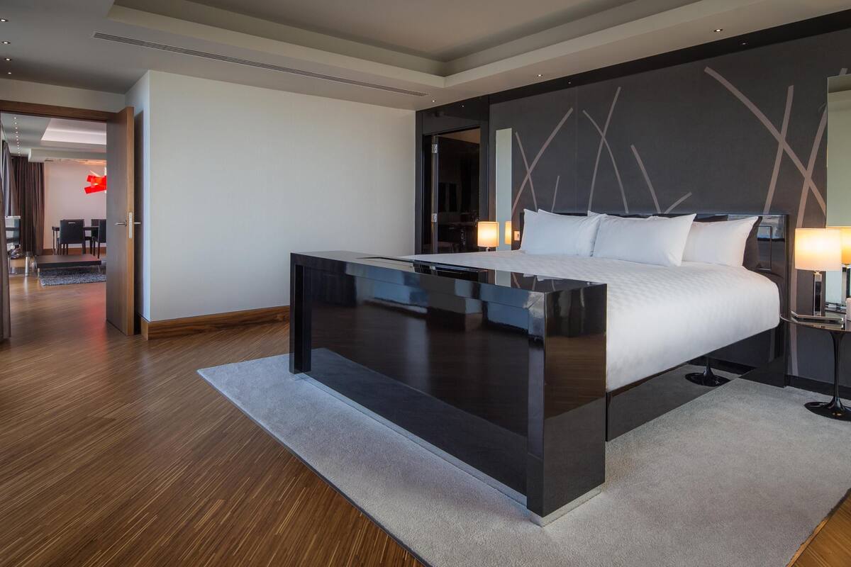 A modern hotel room with a large bed, bedside tables, a desk, and a view of the hallway.