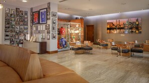 Een hotel lobby met een receptiebalie, ingelijste foto's aan de muur, een zithoek met moderne stoelen, en een groot schilderij van een stadsgezicht.