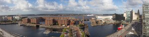 Stadsgezicht aan het water met historische gebouwen, een modern glazen gebouw en een drukke haven met boten en een veerboot.