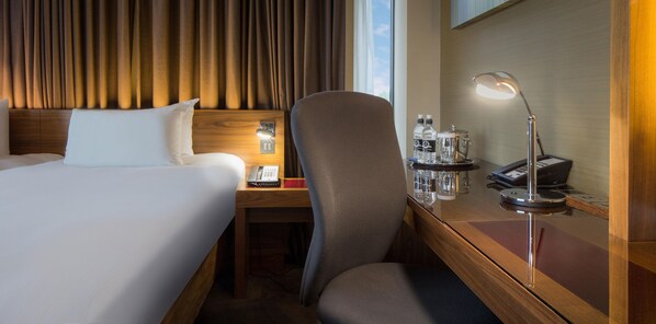 A hotel room with a bed, a desk with a lamp, a chair, and a telephone.