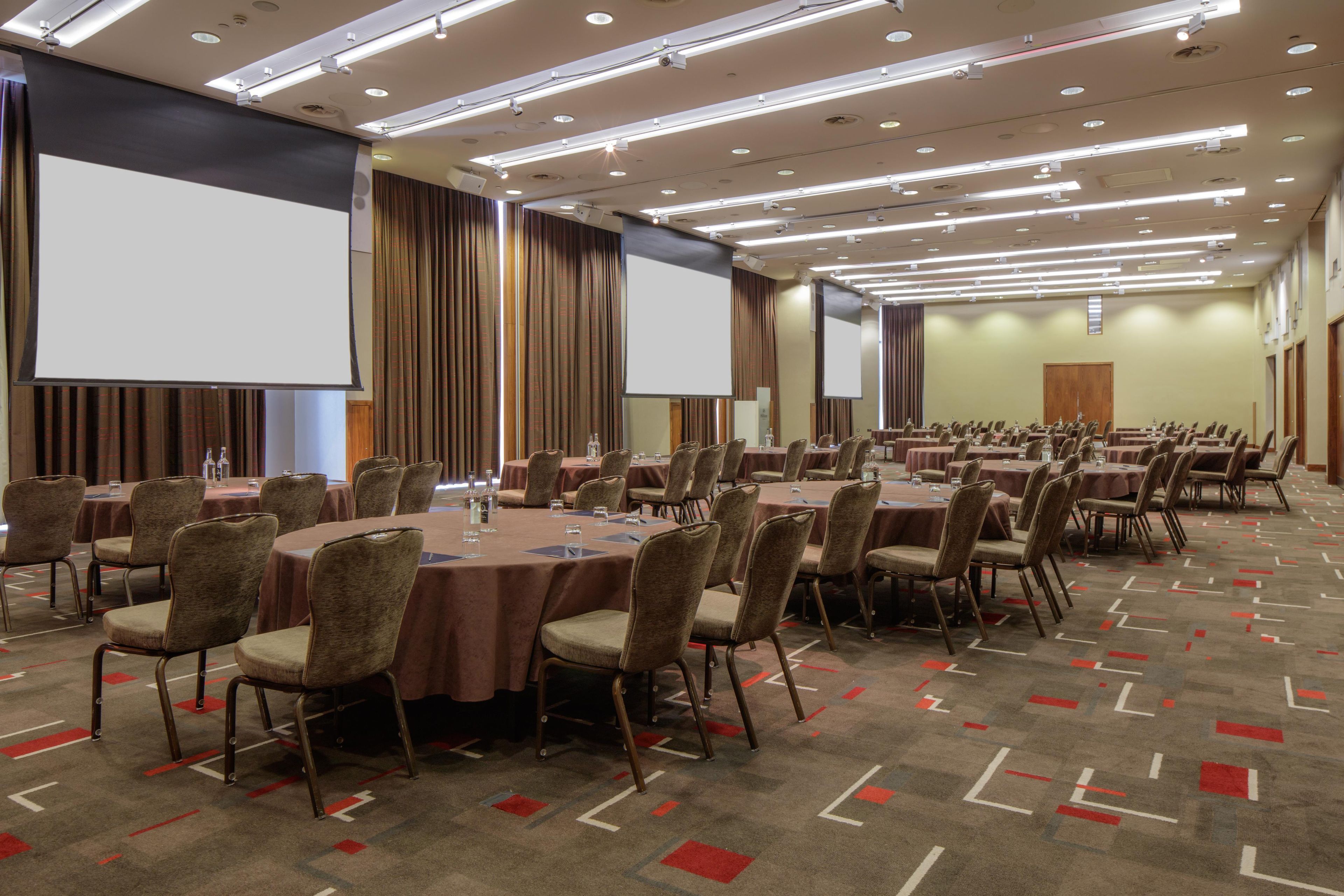 A conference room with multiple tables and chairs, equipped with projectors and screens.