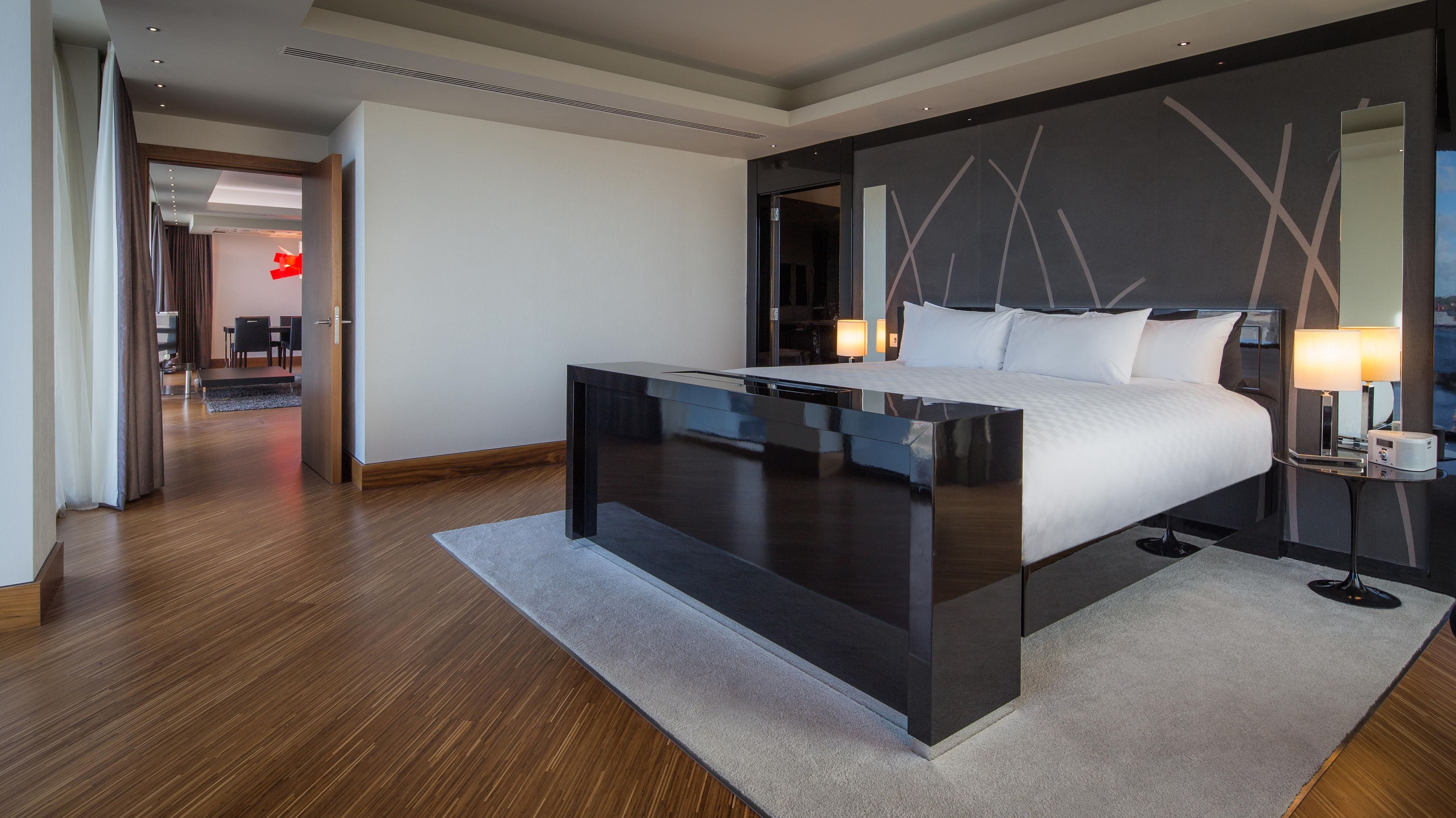 Una habitación de hotel moderna con una cama grande, mesitas de noche, un escritorio y vistas al pasillo.