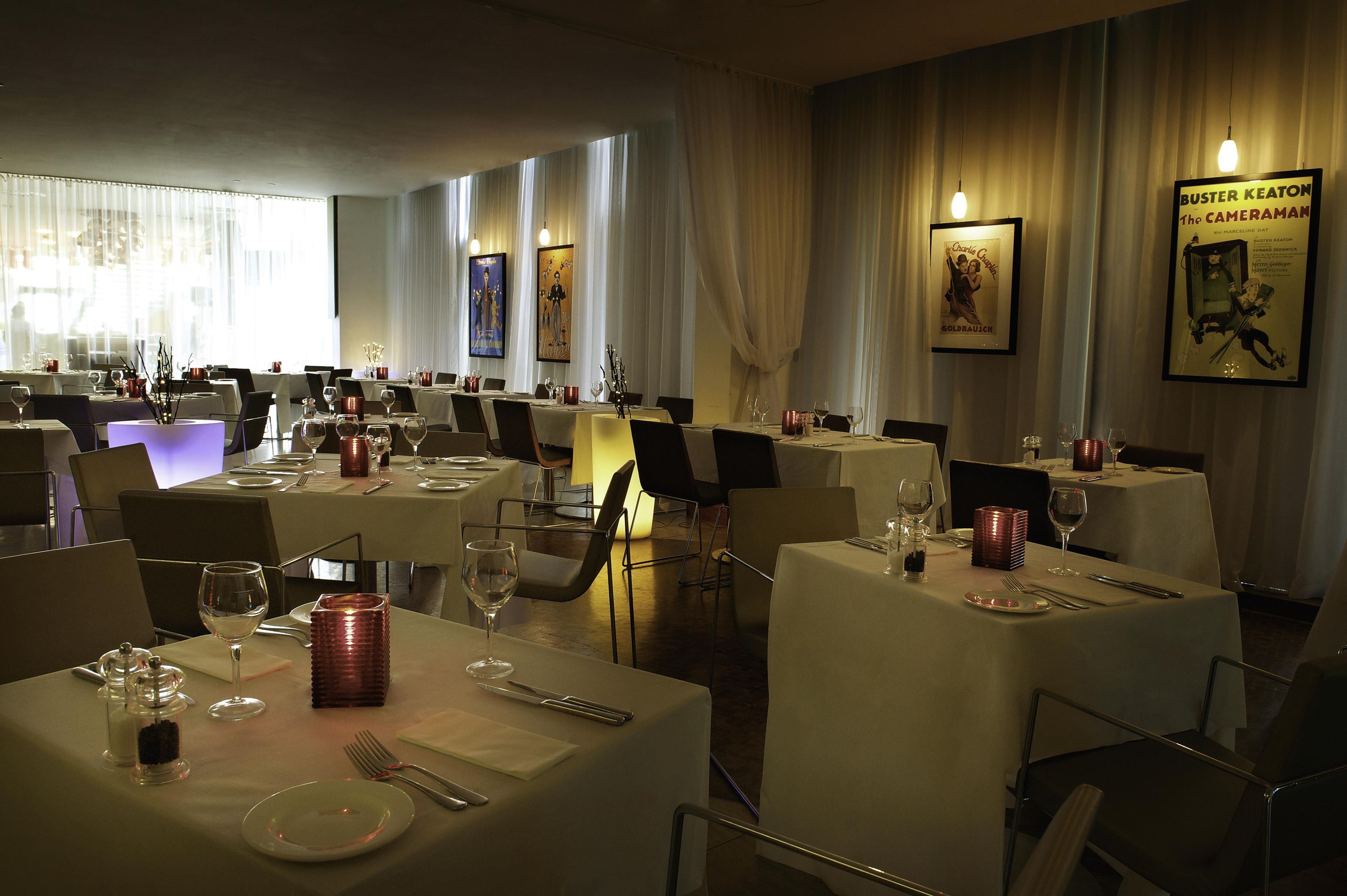 A restaurant with multiple tables set for dining, featuring a classic interior design with curtains and framed artwork on the walls.
