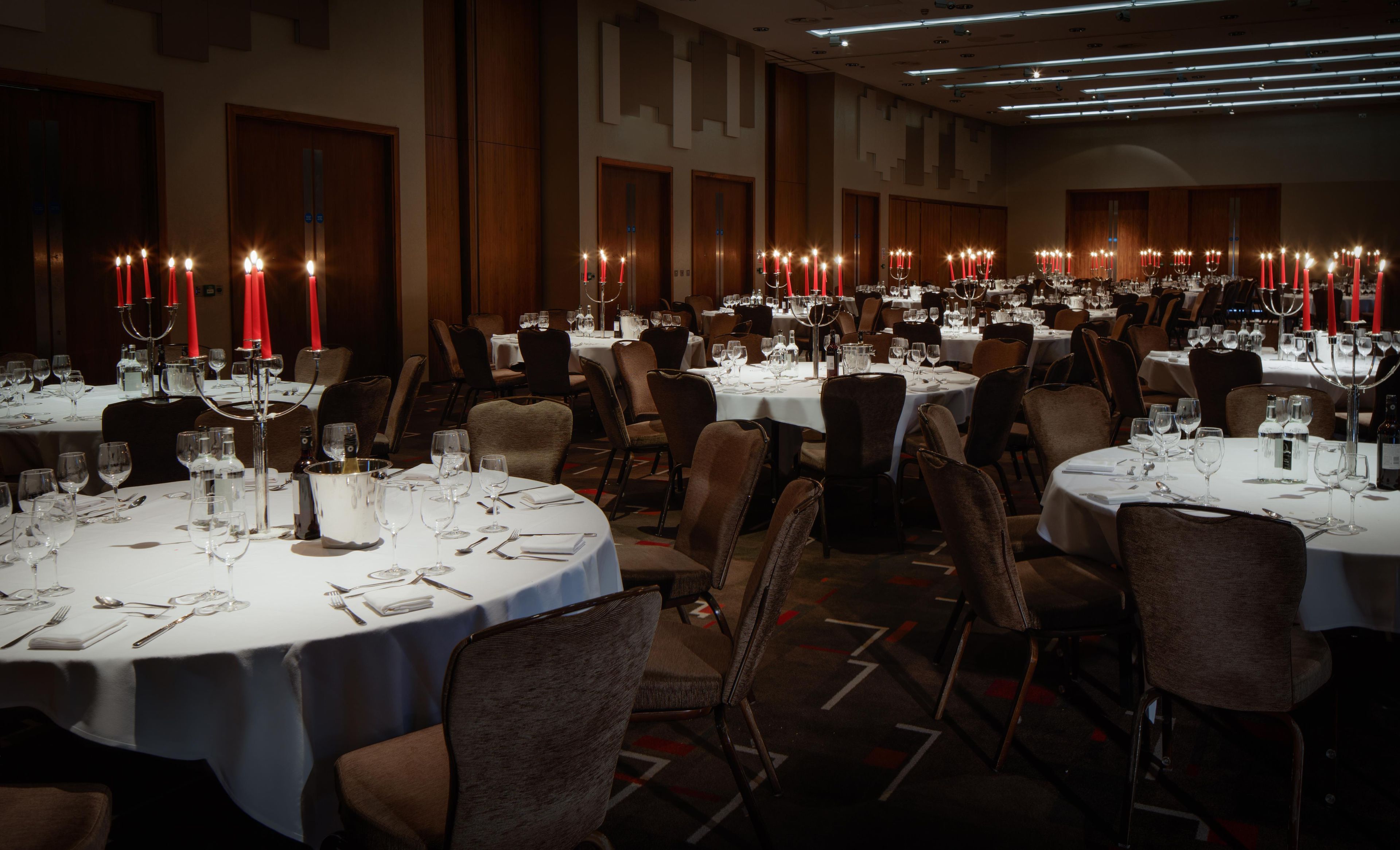 Ein Festsaal mit runden Tischen, gedeckt für ein Essen, jeder Tisch mit einem Kerzenständer und Weingläsern.