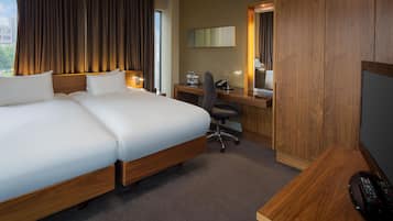 A hotel room with a large bed, a desk with a computer, a chair, a TV, and a window with curtains.
