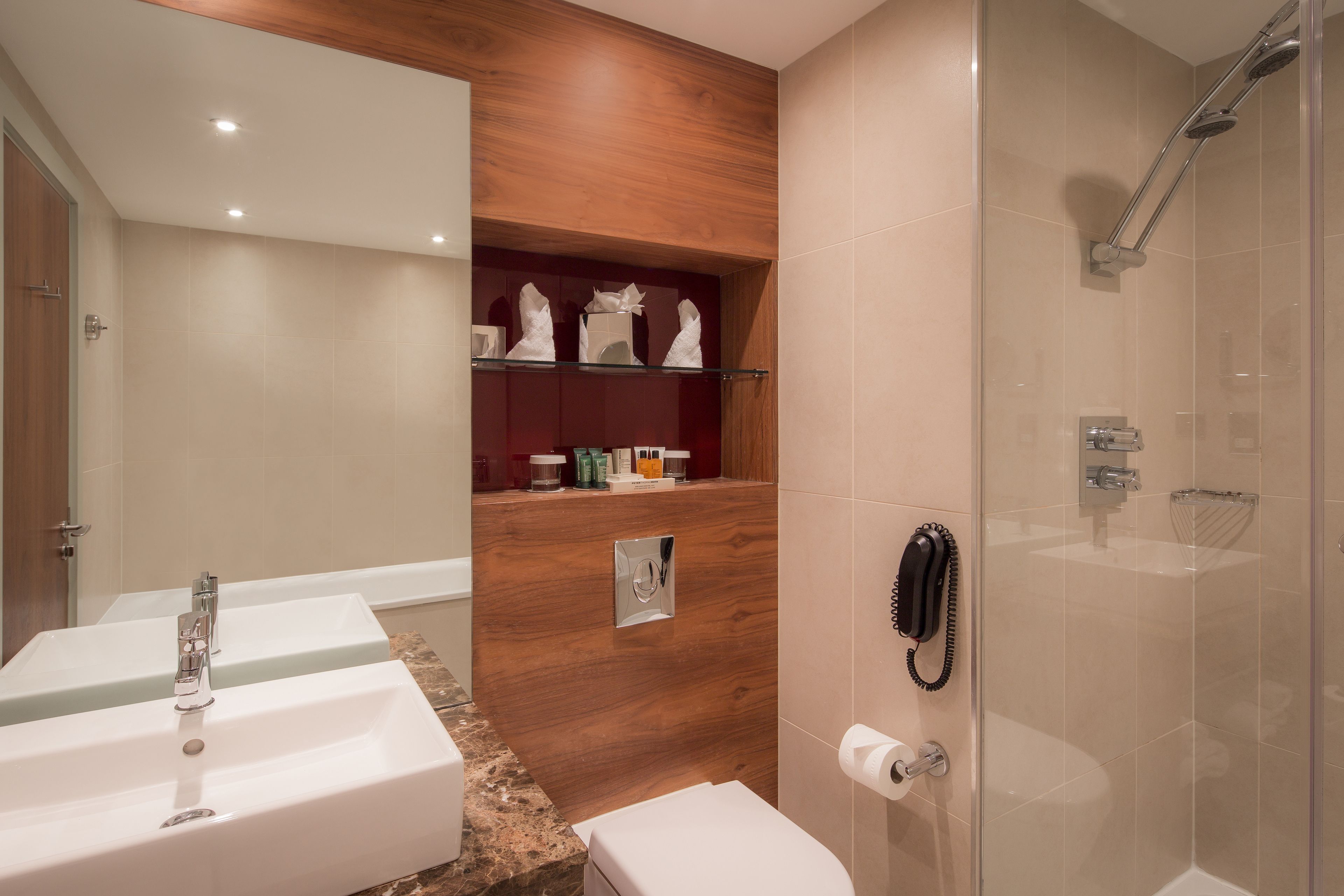 A modern bathroom with two sinks, a shower, and a wooden vanity with toiletries.