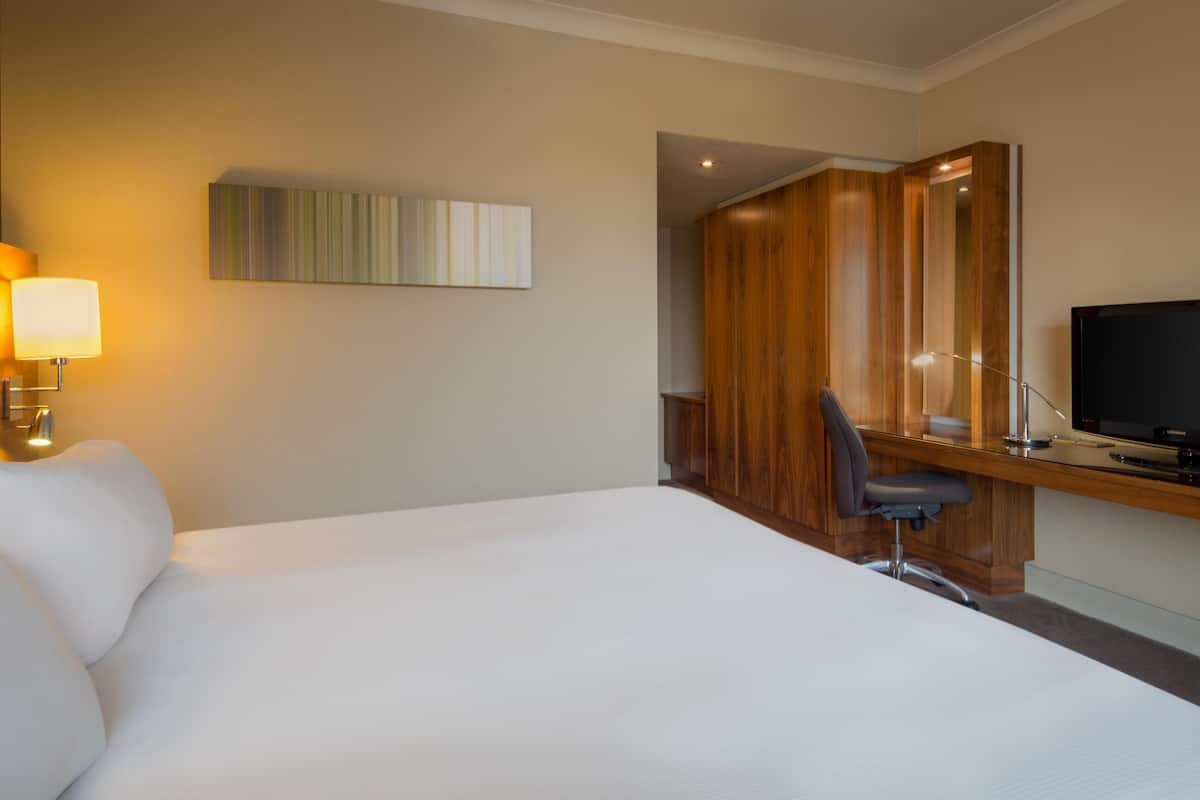 A hotel room with a large bed, a desk with a chair, a television, and a lamp.