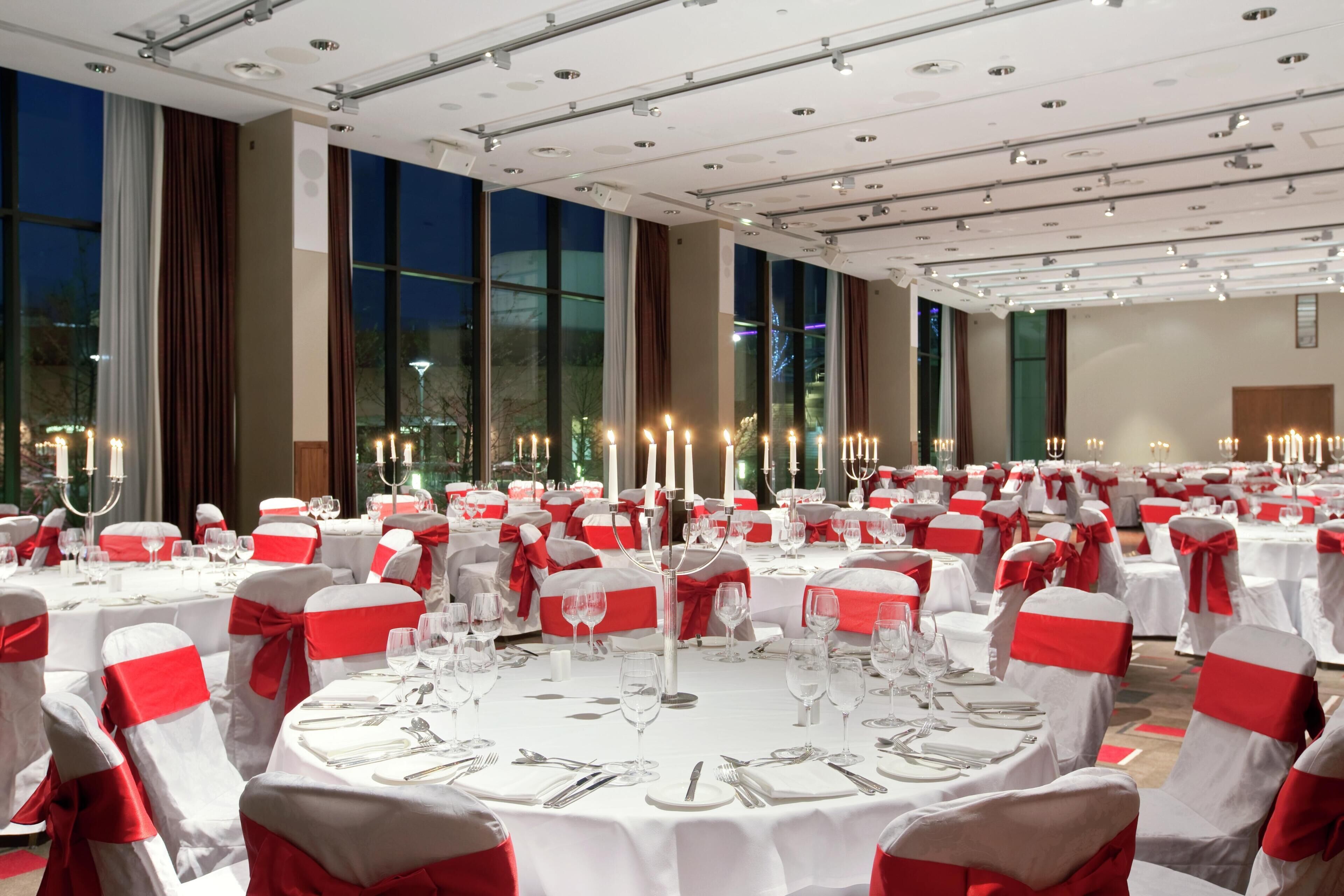 A banquet hall with round tables, white tablecloths, and red sashes on chairs.