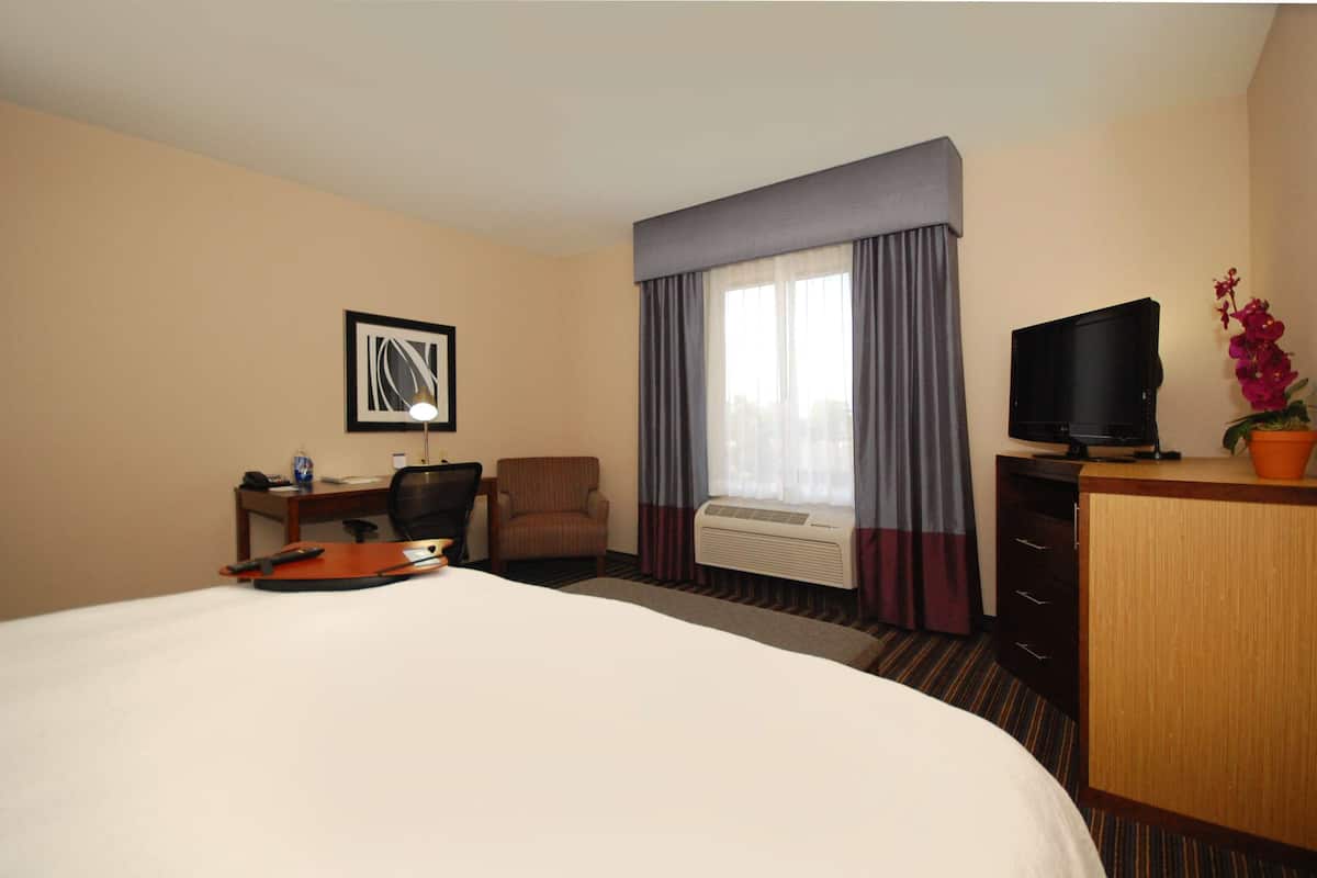 A hotel room with a large bed, a desk with a chair, a television, and a window with curtains.