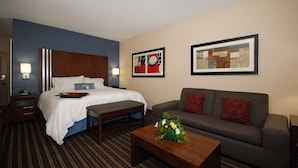 A hotel room with a bed, a sofa, a coffee table, and artwork on the walls.