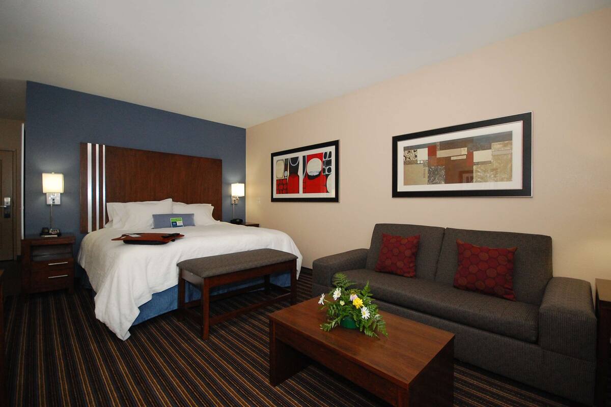 A hotel room with a bed, a sofa, a coffee table, and artwork on the walls.