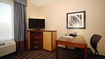 Hotelkamer met een flatscreen televisie, een bureau met lamp, een stoel, een garderobe en een groot raam met gordijnen.