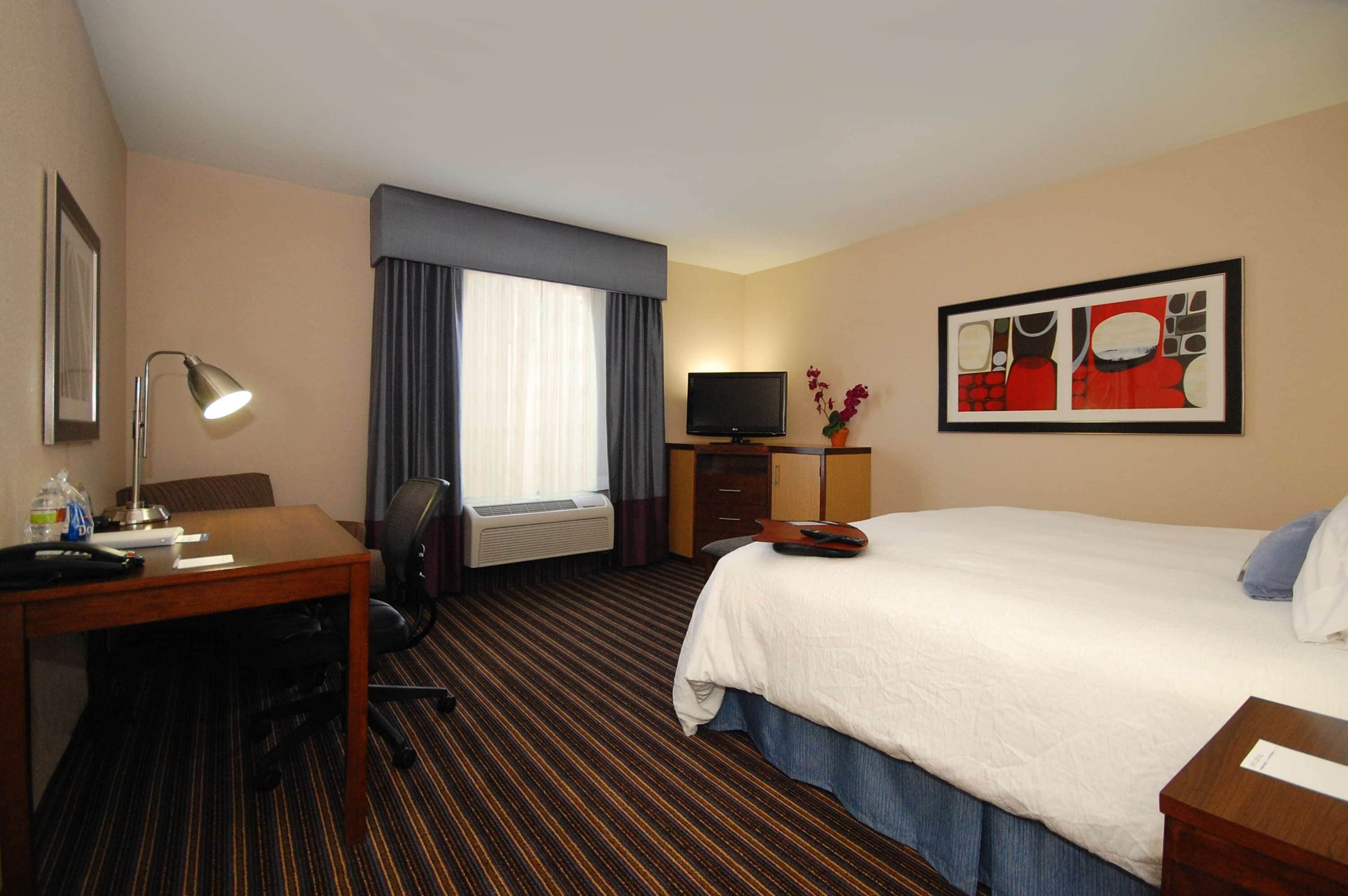Une chambre d’hôtel avec un lit, un bureau doté d’une lampe, une télévision et une petite table sur laquelle est posé un vase.
