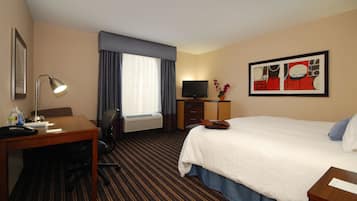 Una habitación de hotel con una cama, un escritorio con lámpara, un televisor y una mesita con un florero.