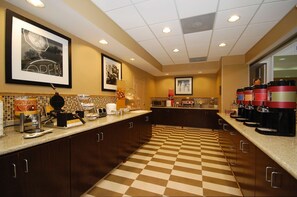 A hotel kitchen with checkered flooring, dark wooden cabinets, and a coffee station with multiple coffee makers.